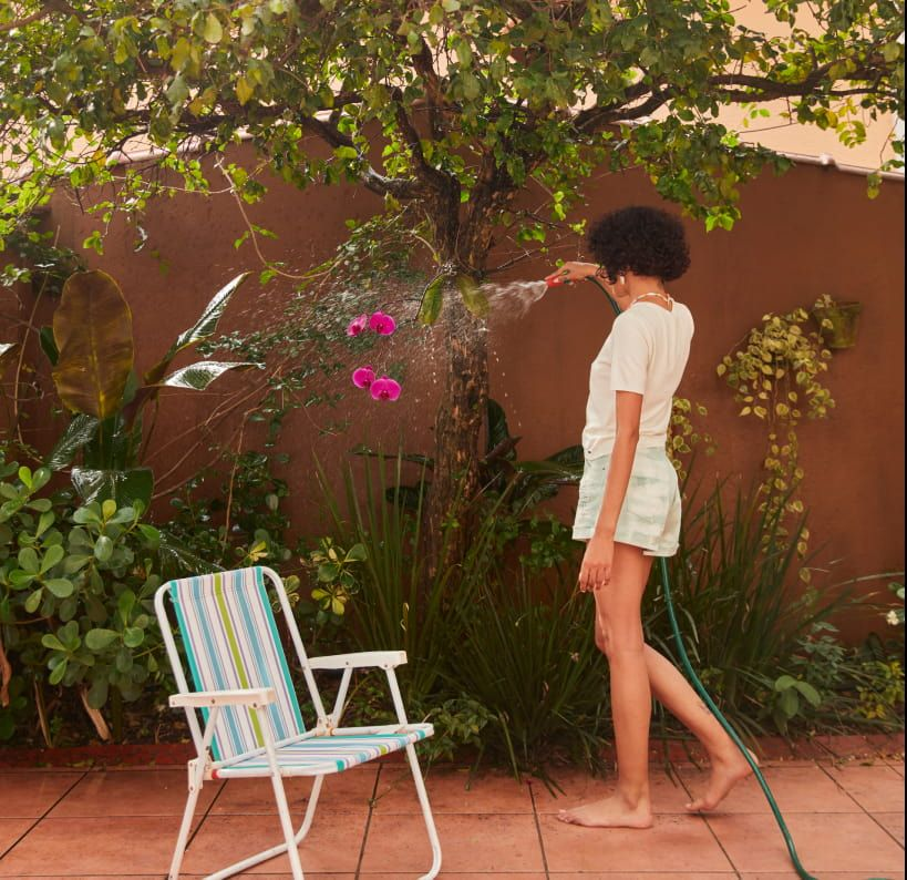 Mulher regando as plantas, com uma cadeira de praia ao lado