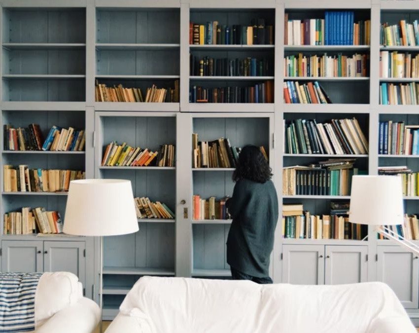 mulher olha para biblioteca em casa, cheia de livros coloridos nas prateleiras