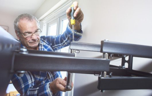 Imagem de um um senhor de óculos instalando um suporte de TV na parede.