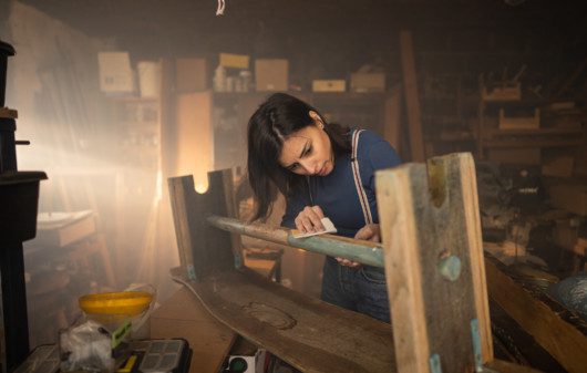 Imagem de uma mulher em um depósito fazendo um banco de madeira.
