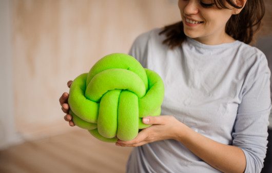 Imagem de uma mulher segurando uma almofada de nó verde.
