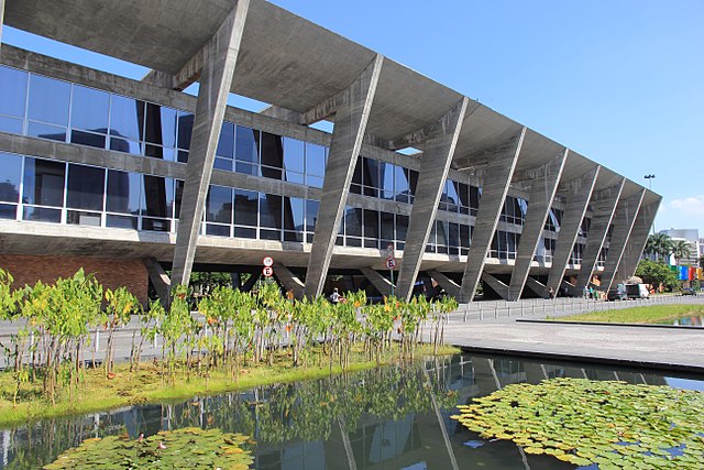 Foto que ilustra matéria sobre museus do Rio de Janeiro mostra a fachada do Museu de Arte Moderna do Rio de Janeiro com seu lago e plantas logo à frente.
