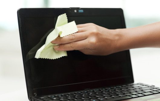 Imagem de uma pessoa limpando a tela de um notebook com uma flanela.