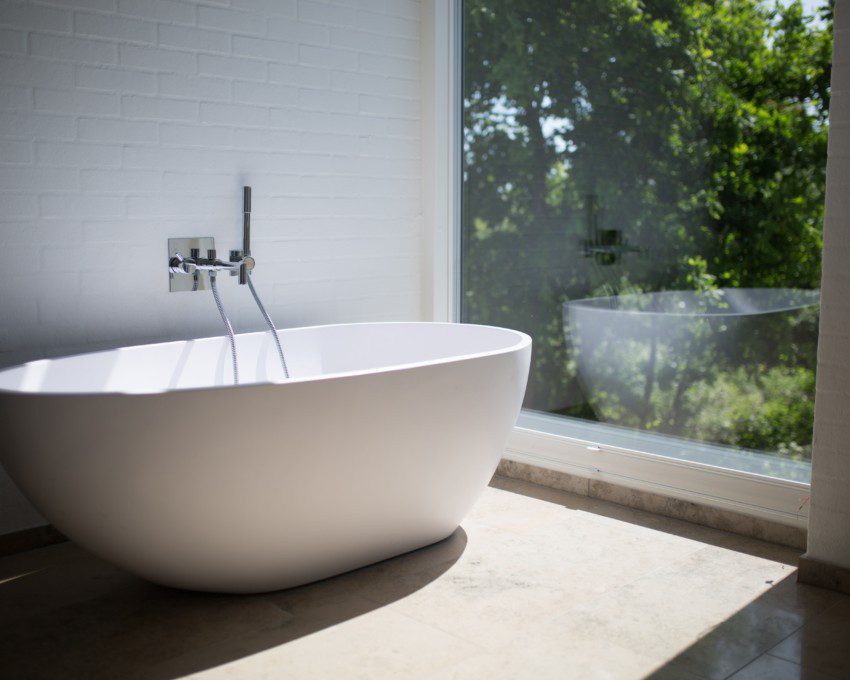 Imagem de banheira de cerâmica branca ao lado de uma parede de vidro.