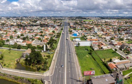 Foto que ilustra matéria sobre os bairros de Pinhais mostra uma panorâmica da cidade, com destaque para a Rodovia Deputado João Leopoldo, a principal via da região.