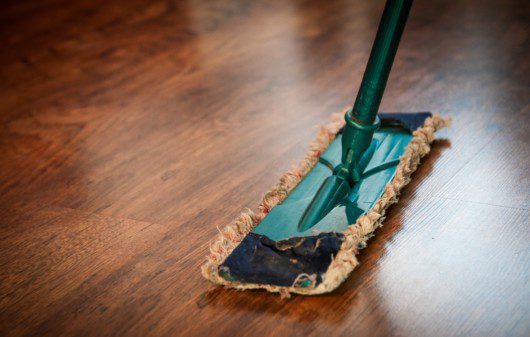 Imagem de uma pessoa limpando um chão com piso de madeira.
