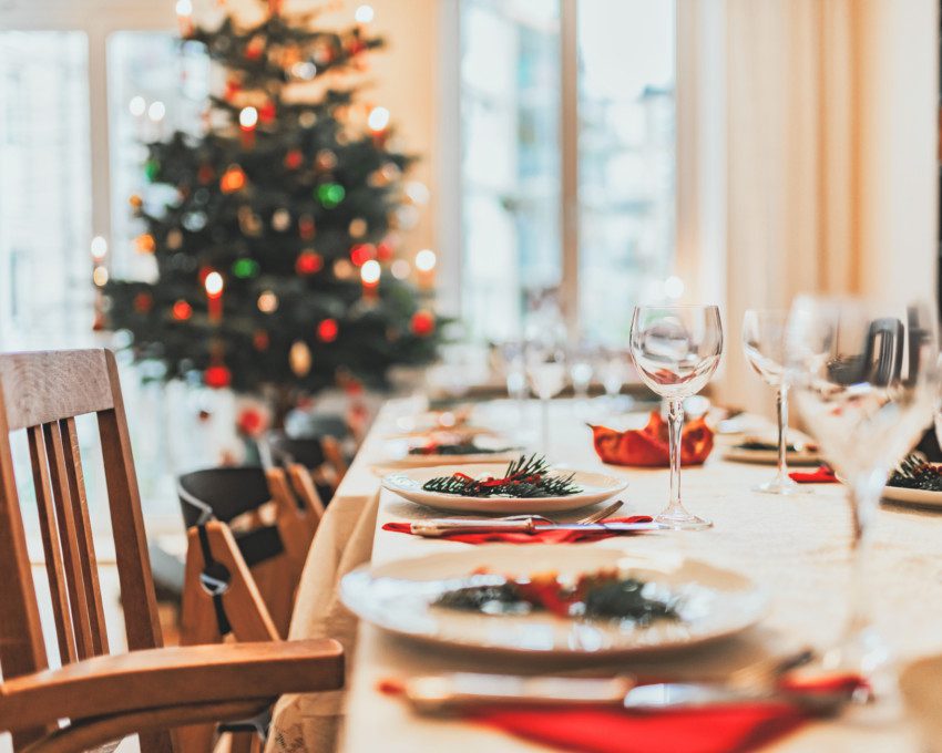 Imagem de uma mesa de Natal posta com uma árvore de Natal ao fundo.