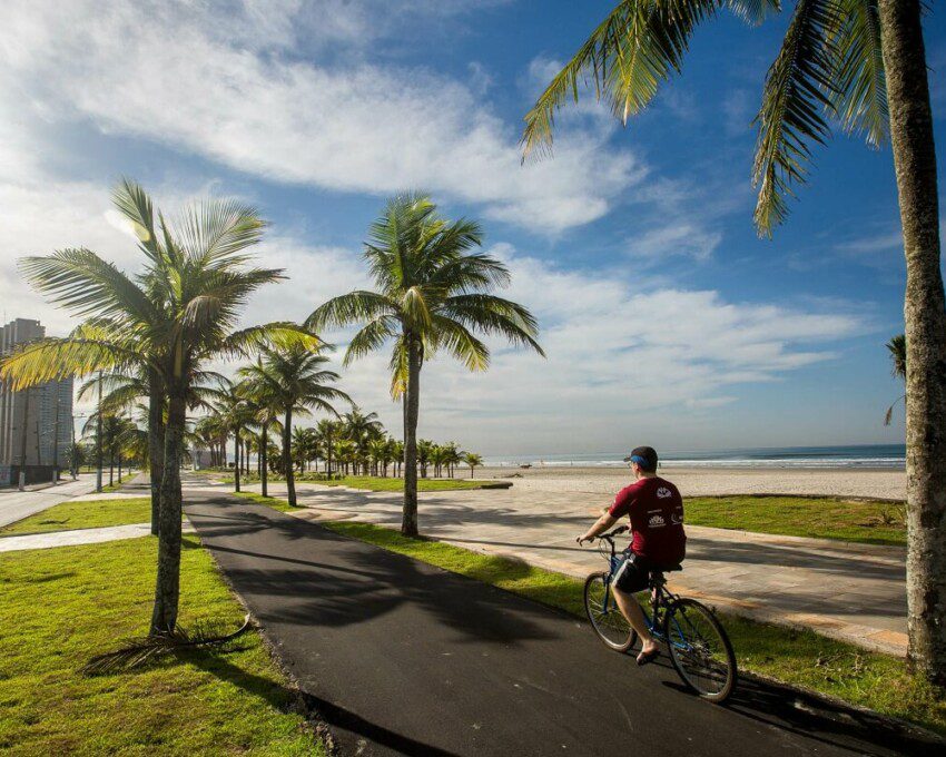 Foto que ilustra matéria sobre o que fazer em Praia Grande mostra um ciclista pedalando na ciclovia da orla de uma das praias da cidade