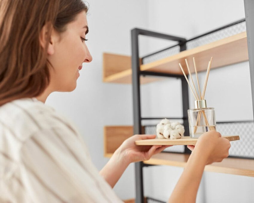 Foto que ilustra matéria com dicas sobre como deixar a casa cheirosa mostra uma mulher posicionando um difisor de aromas em uma estante