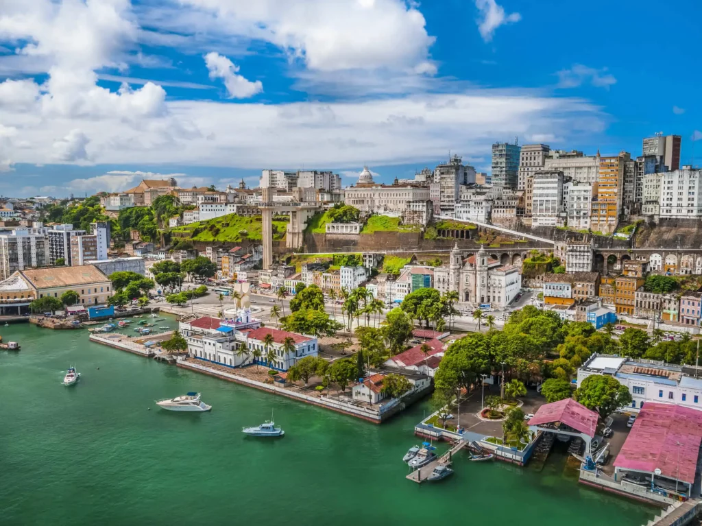 Imagem da vista aérea de Salvador mostra barcos, mar, prédios e vegetação em um dia de céu azul para ilustrar matéria sobre os bairros mais populosos da capital baiana