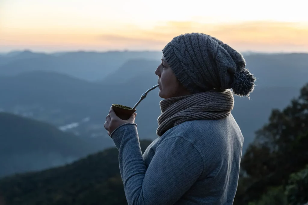 Imagem de uma mulher com touca, cachecol e blusa de frio, tomando um chimarrão enquanto admira a paisagem das montanhas em um dia frio para ilustrar matéria sobre a cidade mais fria do Rio Grande do Sul