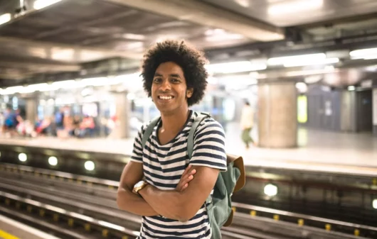 Imagem de um homem jovem sorrindo enquanto aguarda o trem em uma estação de metrô para ilustrar matéria sobre Linha 8-Diamante