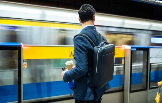 Imagem de um homem usando terno com uma mochila nas costas em uma estação de metrô esperando o trem para ilustrar matéria sobre a Linha Amarela do metrô de SP