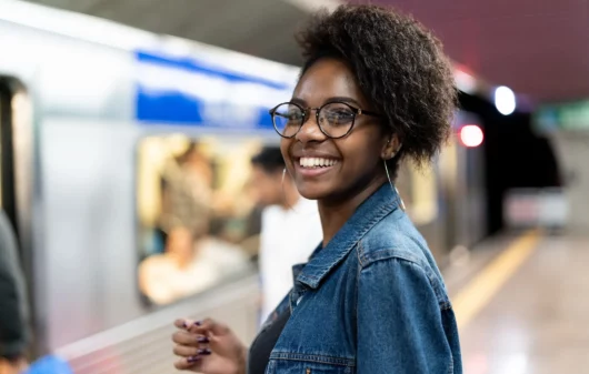 Imagem de uma mulher negra sorrindo em uma estação de metrô aguardando o trem abrir as portas para ilustrar matéria sobre a Linha 1-Azul do metrô de SP