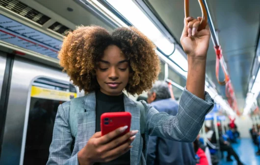 Imagem de uma mulher negra em pé em um metrô segurando na barra de segurança enquanto olha para a tela do celular para ilustrar matéria sobre a Linha Verde do metrô de SP