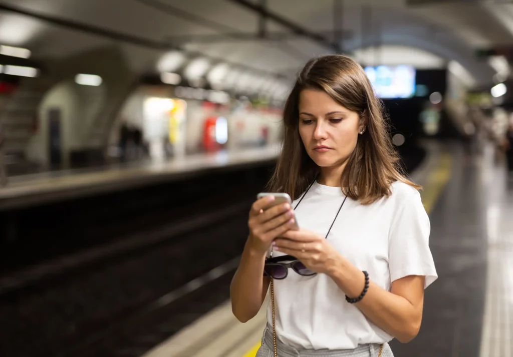 Imagem de uma mulher usando o celular em uma estação de metrô enquanto aguarda o trem para ilustrar matéria sobre mapa da Linha 1-Azul, do metrô de São Paulo