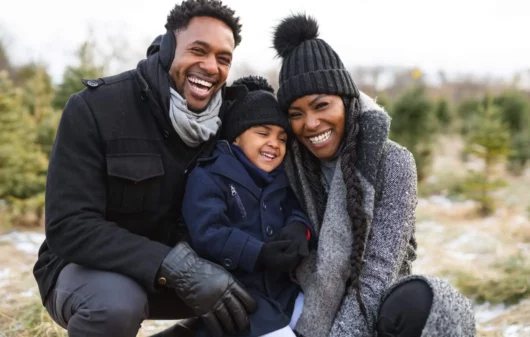 Imagem de uma família formada por um homem, uma mulher e uma criança sorrindo e agasalhada com touca, cachecol e luva para ilustrar matéria sobre qual a cidade mais fria do Nordeste