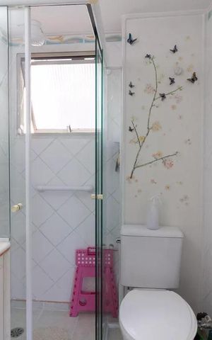 Apartamento à venda com 77m², 3 quartos e 1 vagaBanheiro com ducha, vaso sanitário e pia, com decoração de borboletas e flores na parede.