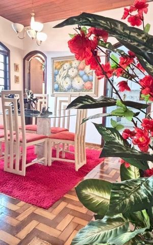 Casa à venda com 170m², 4 quartos e 5 vagasSala de jantar com mesa de vidro e cadeiras brancas e vermelhas, com um tapete vermelho e uma planta com flores vermelhas na frente.