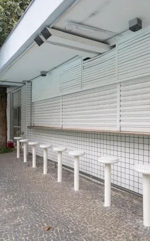 Apartamento à venda com 60m², 2 quartos e 2 vagasPavimentação de pedras e bancos de concreto em frente a uma construção branca.
