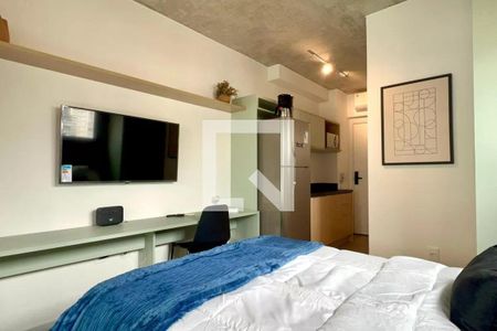 Quarto com cama, TV e mesa de trabalho, com uma cozinha pequena ao fundo. de apartamento à venda com 1 quarto, 24m² em Pompeia, São Paulo