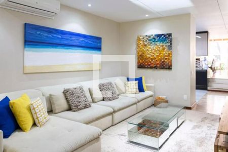 Sala de estar com sofá branco, pinturas em tons de azul e amarelo, e mesa de vidro. de casa à venda com 6 quartos, 280m² em Cerqueira César, São Paulo