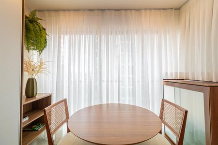 Apartamento à venda com 28m², 1 quarto e sem vagaTabela redonda de madeira com cadeiras de madeira e cana, com cortinas claras e um armário de madeira.