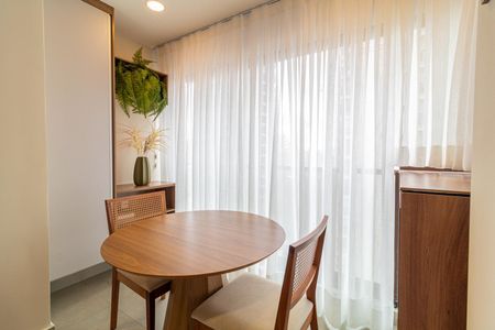 Apartamento à venda com 28m², 1 quarto e sem vagaTabela redonda de madeira com duas cadeiras, com uma janela com cortinas claras e um armário com uma planta de ferns.