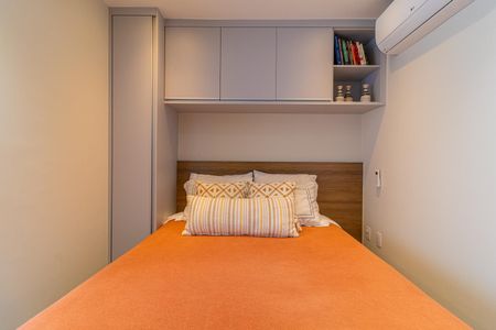 Apartamento à venda com 28m², 1 quarto e sem vagaCama com cabeceira de madeira e colchão de cor laranja, com prateleiras acima e ar condicionado na parede.