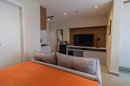 Cama com colchão e cobertor, sofá e TV na parede, cozinha com geladeira e fogão, e uma porta de entrada. de apartamento à venda com 1 quarto, 28m² em Vila Nova Conceição, São Paulo