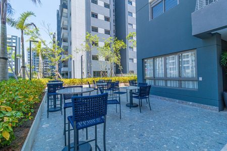 Apartamento à venda com 69m², 2 quartos e 1 vagaPatio com mesas e cadeiras azuis, cercado por plantas e edifícios de apartamentos.