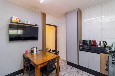Casa à venda com 130m², 2 quartos e 4 vagasCozinha com mesa de madeira e televisão na parede, com geladeira e fogão na bancada de granito.