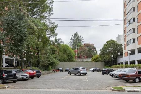 Apartamento à venda com 60m², 2 quartos e 2 vagasPraça de estacionamento com vários carros, árvores e edifícios ao redor.