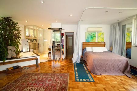 Casa à venda com 400m², 4 quartos e 6 vagasQuarto com cama, piso de madeira e móveis simples, com uma planta no canto e uma porta para o banheiro.