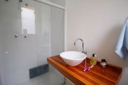 Casa à venda com 400m², 4 quartos e 6 vagasBanheiro com pia e chuveiro, com uma mesa de madeira e um espelho.