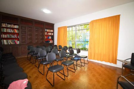 Casa à venda com 400m², 4 quartos e 6 vagasSala com móveis de madeira, prateleiras de livros e janelas com cortinas amarelas.