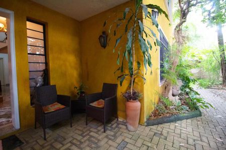Casa à venda com 400m², 4 quartos e 6 vagasPatio com duas cadeiras de vime e uma planta em um vaso de barro, com uma parede amarela e um chão de tijolos.