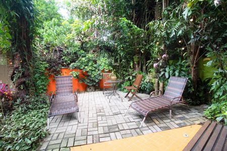 Casa à venda com 400m², 4 quartos e 6 vagasPatio com duas cadeiras de praia e uma mesa pequena, cercado por plantas e árvores.