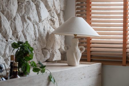 Apartamento à venda com 160m², 2 quartos e 3 vagasLâmpada de mesa com design único e iluminação suave, em uma sala com paredes de pedra e janela com persianas de madeira.