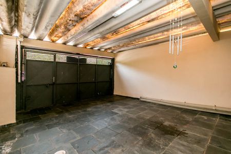 Casa à venda com 180m², 4 quartos e 2 vagasGaragem com portas de metal e piso de pedra, iluminada por luzes fluorescentes.