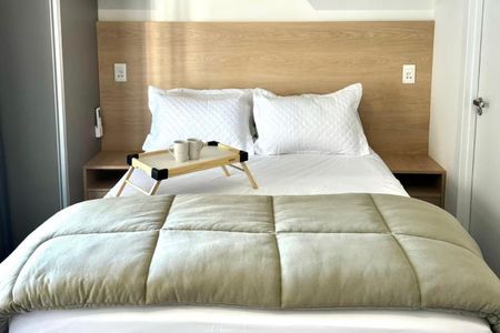 Cama simples com colchão branco e cabeceira de madeira, com uma mesa de serviço com duas xícaras de café. de kitnet/studio à venda com 1 quarto, 26m² em Bela Vista, São Paulo