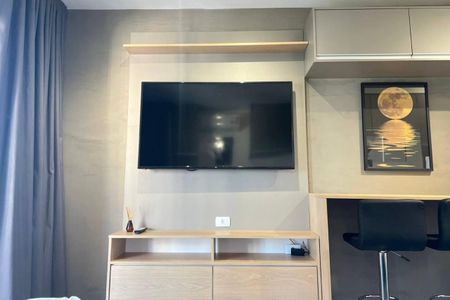 Studio à venda com 26m², 1 quarto e sem vagaTelevisão de tela grande em parede com prateleira acima e baixo, com móveis de madeira claro e iluminação adequada.