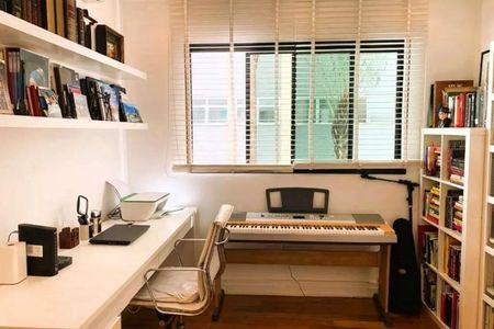 Apartamento à venda com 246m², 4 quartos e 3 vagasEscritório com mesa de trabalho, cadeira e piano, com janela e prateleiras de livros.