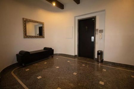 Apartamento à venda com 244m², 6 quartos e 3 vagas Apartamento à venda com 244m², 6 quartos e 3 vagasParede branca com porta de elevador e sofá preto, com espelho emoldurado na parede.