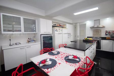 Apartamento à venda com 244m², 6 quartos e 3 vagas Apartamento à venda com 244m², 6 quartos e 3 vagasCozinha com móveis brancos e vermelhos, iluminada por luzes brancas, com uma mesa de jantar com toalha vermelha e pratos brancos, e uma geladeira e fogão brancos.