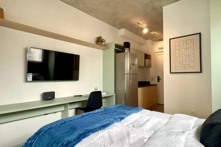 Apartamento à venda com 24m², 1 quarto e sem vagaQuarto com cama, TV e mesa de trabalho, com uma cozinha pequena ao fundo.