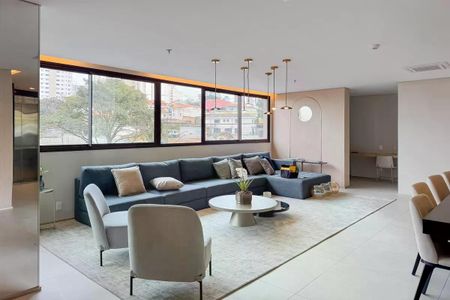 Sala de estar com sofá azul e janelas grandes, iluminada por lâmpadas suspensas. de apartamento para alugar com 1 quarto, 28m² em Ipiranga, São Paulo