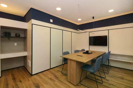 Sala de reuniões com mesa de madeira e cadeiras azuis, iluminação natural e TV na parede. de kitnet/studio à venda com 1 quarto, 28m² em Pinheiros, São Paulo