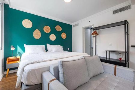 Quarto com cama de casal e sofá, paredes em verde e decoração de folhas de palmeira. de kitnet/studio à venda com 1 quarto, 31m² em Pinheiros, São Paulo