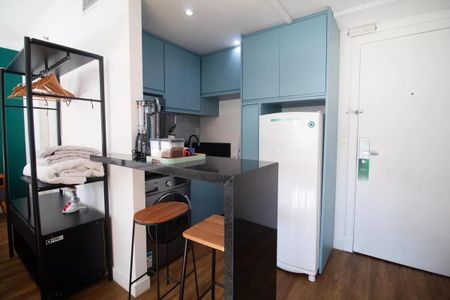 Cozinha com geladeira, fogão e lavadora, com móveis azuis e madeira, e uma mesa com duas cadeiras. de kitnet/studio à venda com 1 quarto, 31m² em Pinheiros, São Paulo
